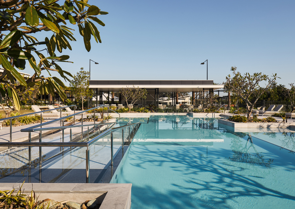 An outdoor resort pool with ramp access, tropical landscaping and a covered barbeque pavilion space.