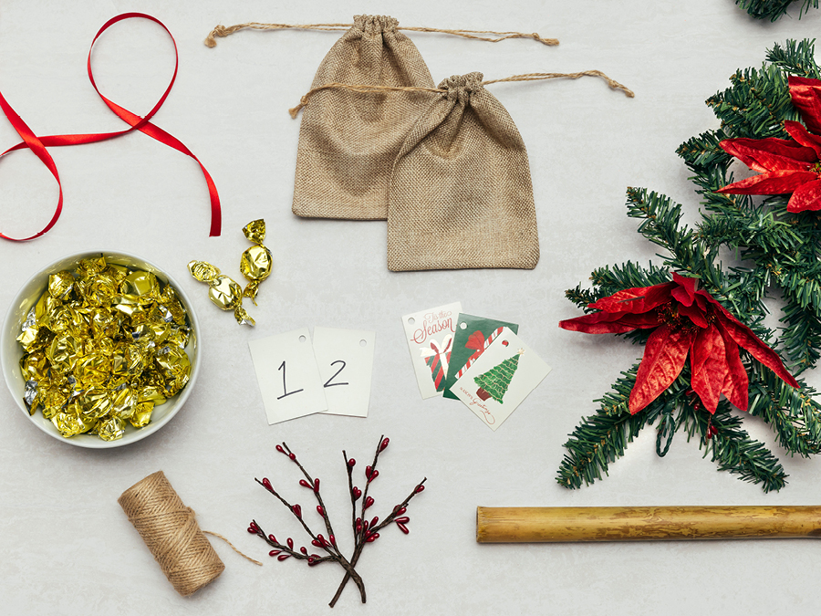 Various items used to create a DIY advent calendar including red ribbon, twine, hessian loot bags, and gift tags.