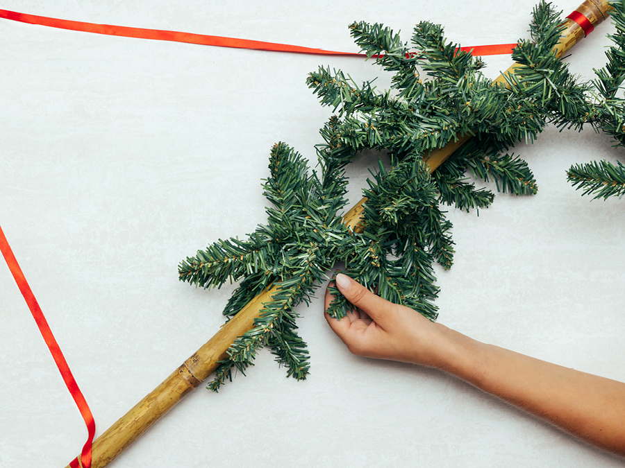 An artificial Christmas garland being wrapped around a bamboo pole.