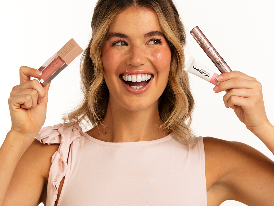 A young woman wearing winter makeup trends, holding various beauty products near her face.