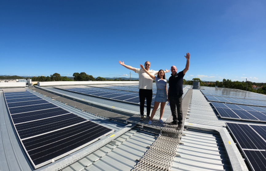 People waving from a building's roof which has solar panels installed