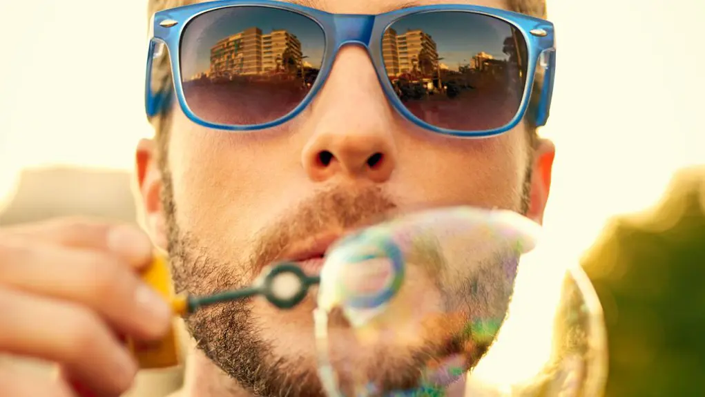 A man wearing shades and blowing out bubbles