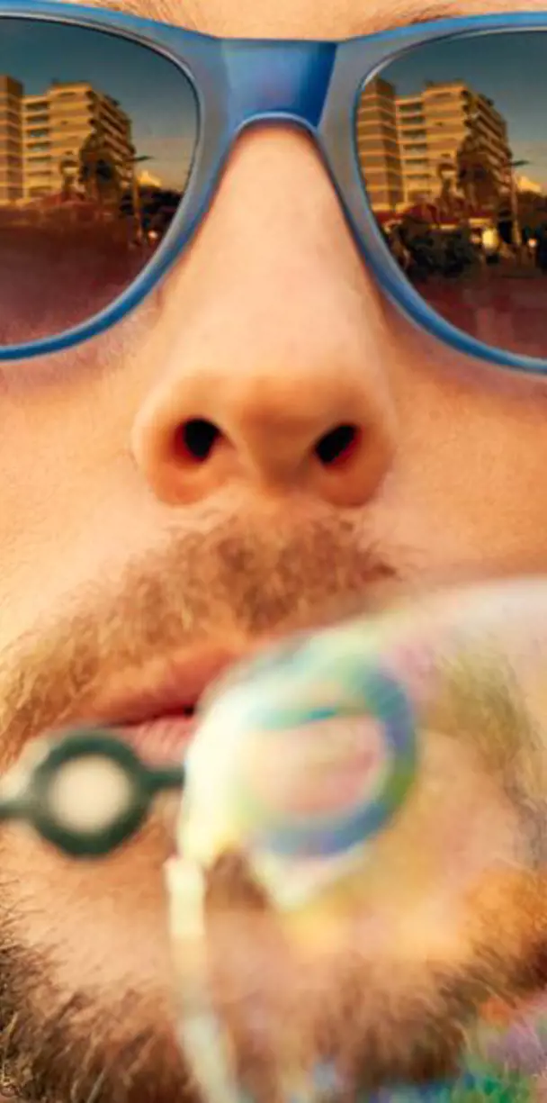 A man wearing shades and blowing out bubbles