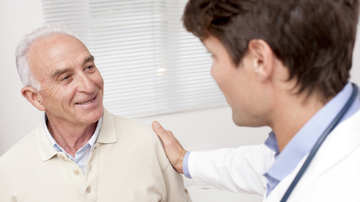 Smiling mature man at doctors surgery with doctor's hand on his shoulder