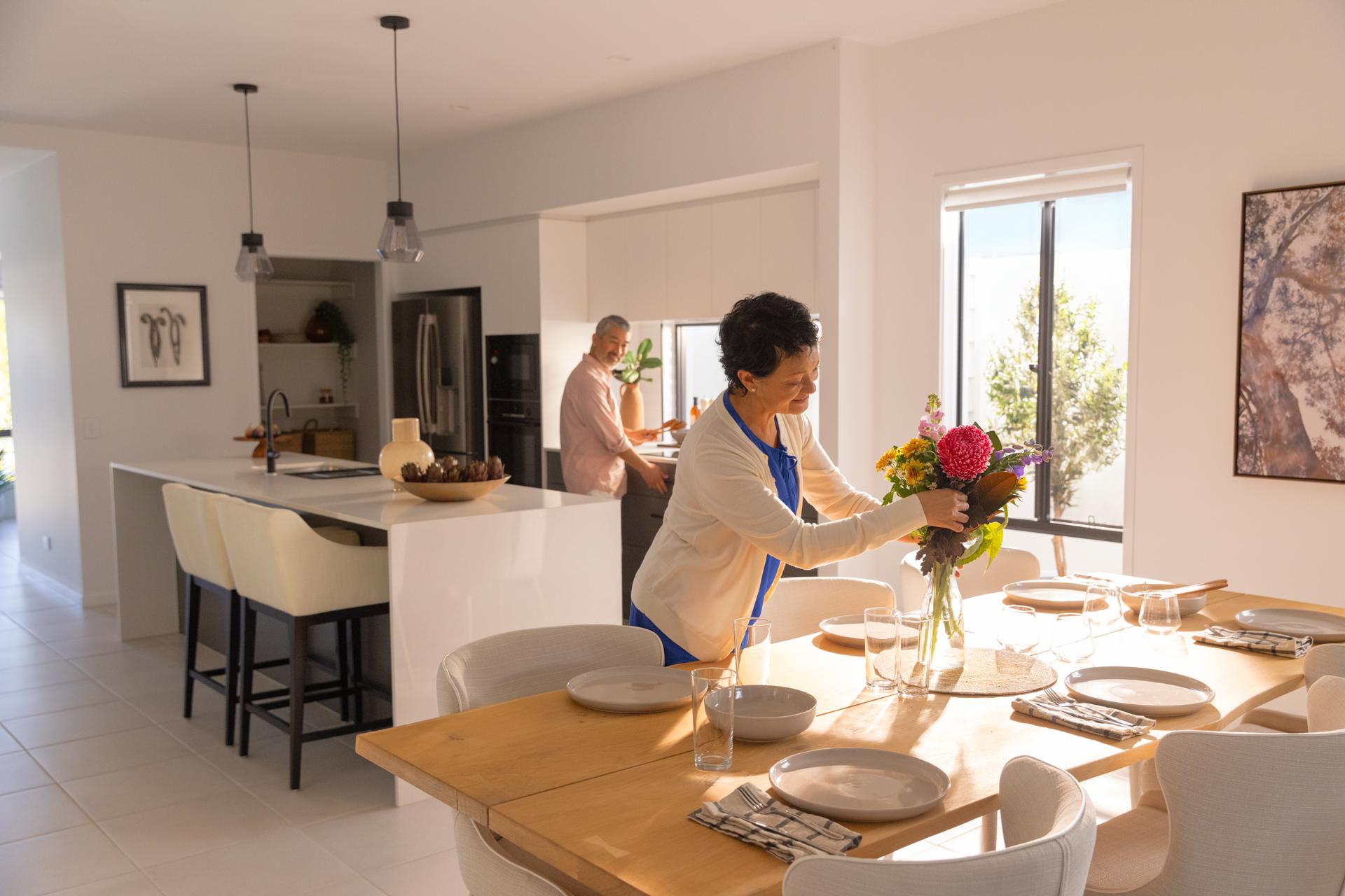 A happy husband and wife in a modern open plan kitchen and dining of a Halcyon home, getting ready to host an afternoon meal.