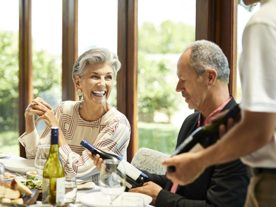 Smiling woman and man looking at wine with waiter at restaurant