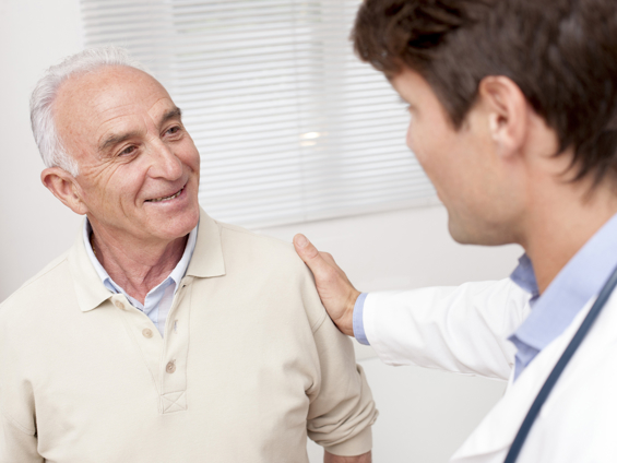 Smiling mature man at doctors surgery with doctor's hand on his shoulder
