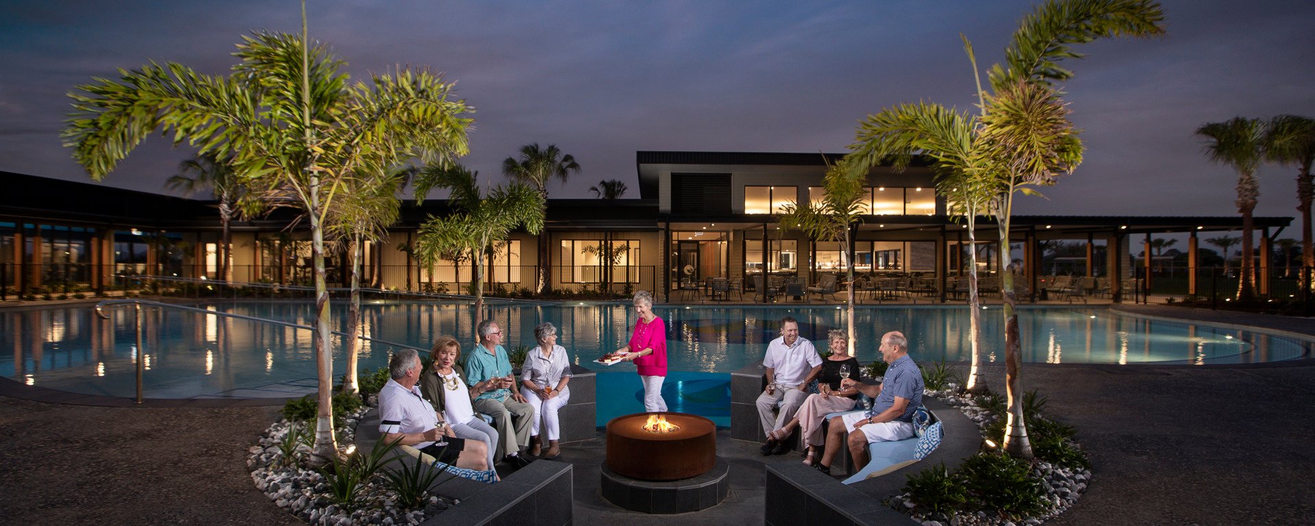Group of Homeowners sitting around the pool side firepit in the evening having drinks and nibbles