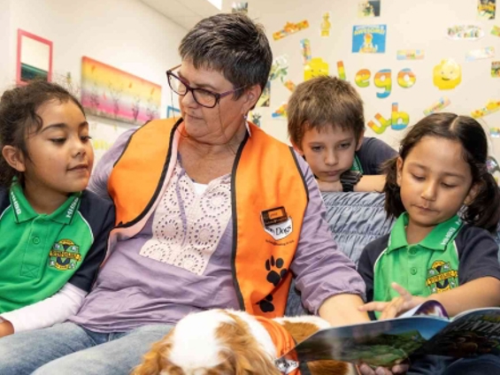 Children reading book with adult and service dog