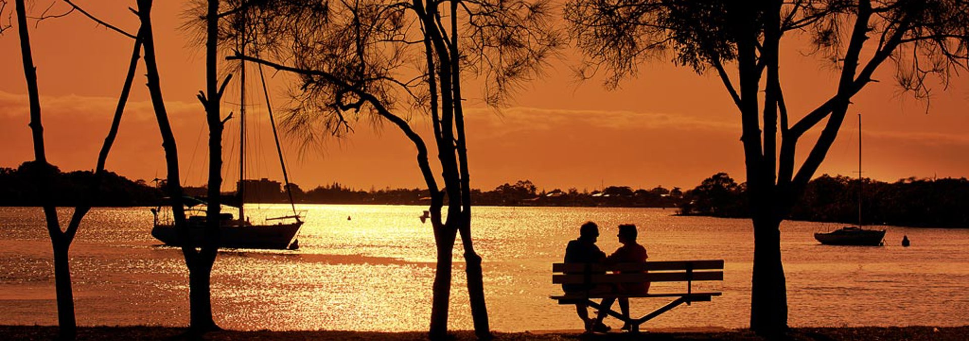 Couple sitting at park bench looking over the water at Hope Island during sunset 