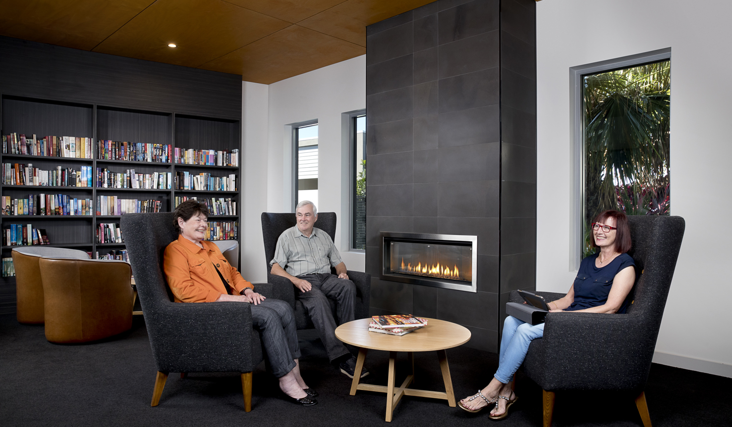 Homeowners sitting and chatting in the library with the fireplace on in the background