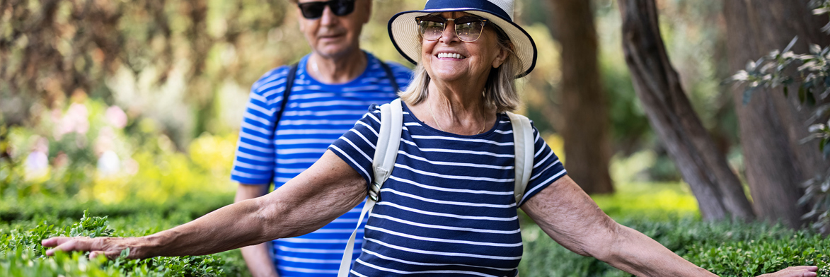 Man and woman walking through nature trail as the lady runs her hand along the shrubs.