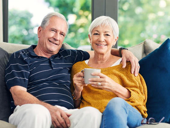 Halcyon Ridge couple sitting on couch smiling, woman holding a mug. 