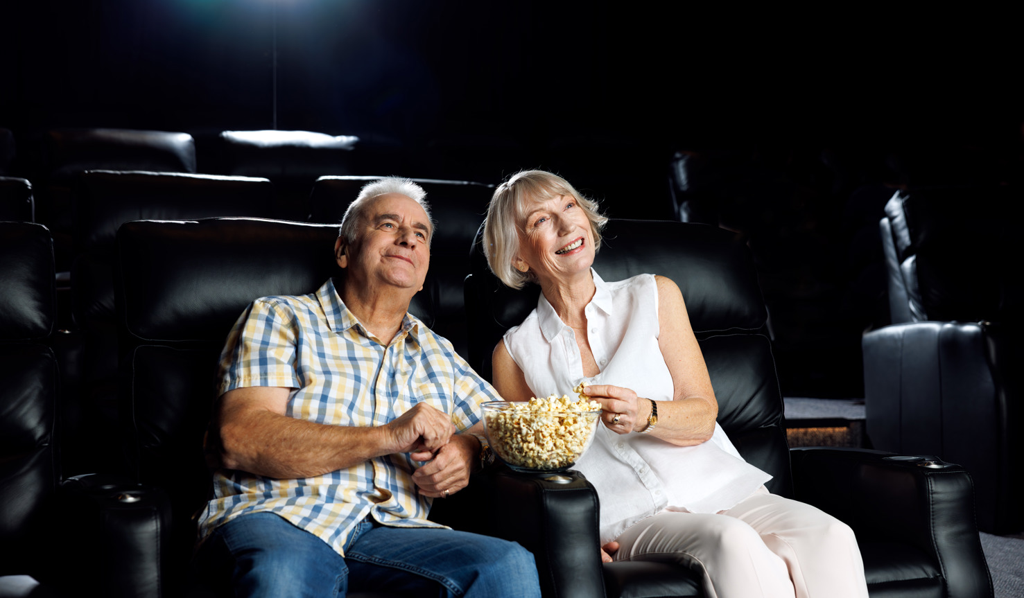 A couple in their 60s enjoying a movie and a bowl of popcorn in the cinema room at Halcyon Rise.