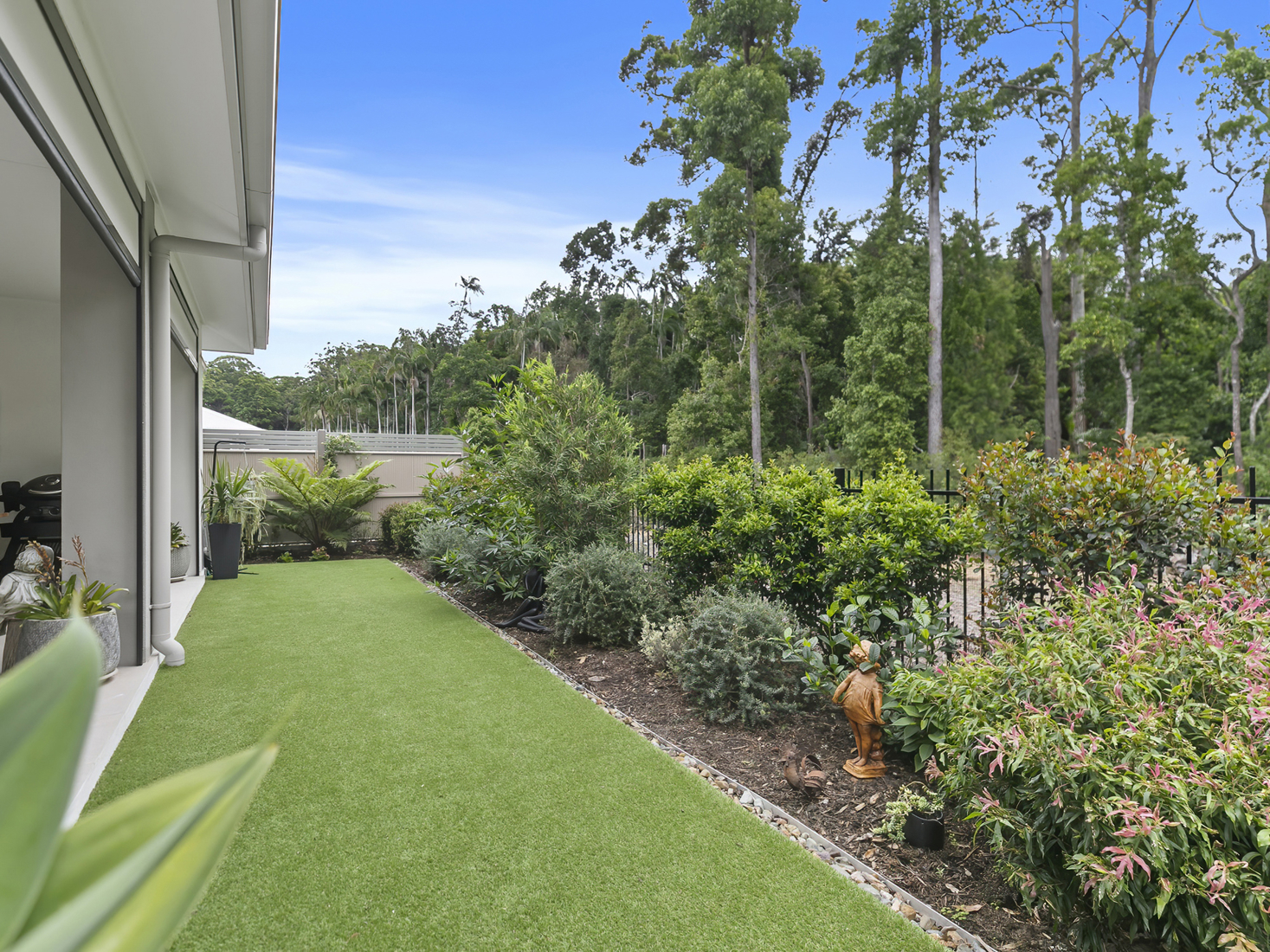 outdoor backyard space with green grass overlooking manicured garden and tropical rainforest background.