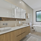light timber bathroom vanity with double sinks and mirrors, beige tiles and white bath tub.