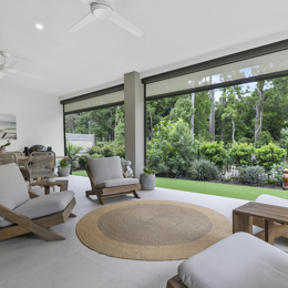 Outdoor covered patio with modern timber lounge setting overlooking lush green garden