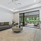 modern lounge room with dark grey sofa, tan rug and round coffee table over looking outdoor green garden.