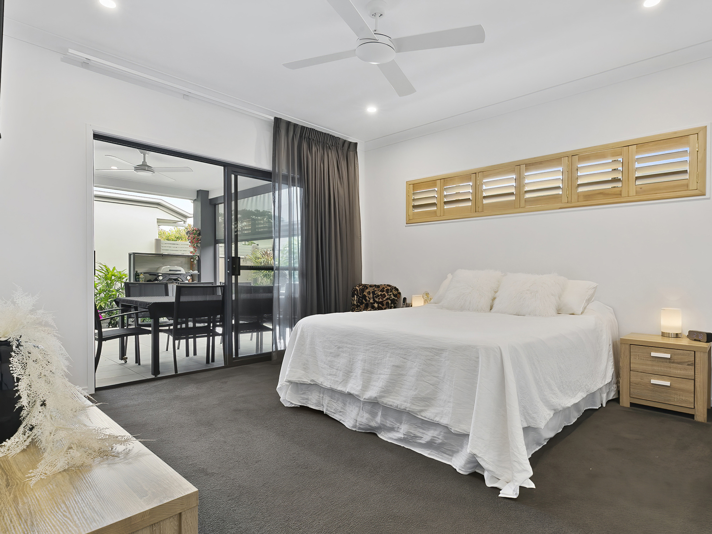 interior image of white bedroom with timber window accents and white bedspread opening up to an outdoor patio.