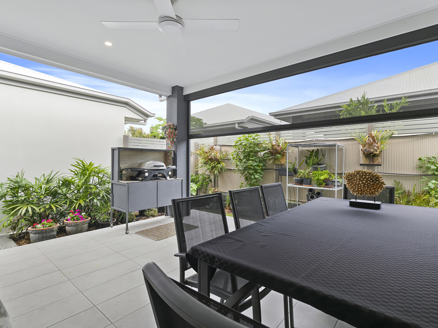 outdoor covered patio area with light tiles, dark dinign setting and barbeque.
