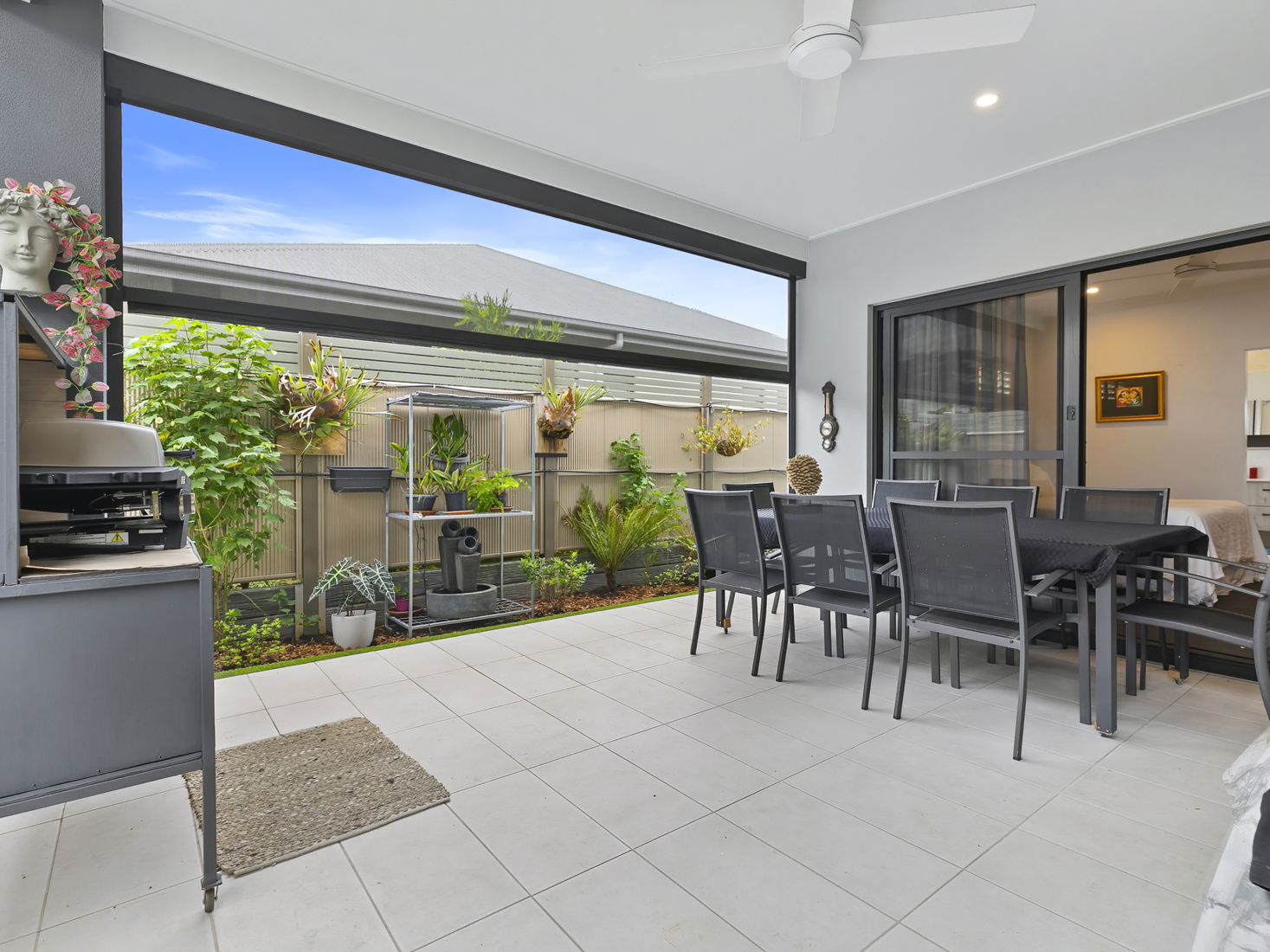 outdoor covered patio with light tiles, white roofline, grey dining setting and barbeque.