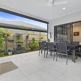 outdoor covered patio with light tiles, white roofline, grey dining setting and barbeque.