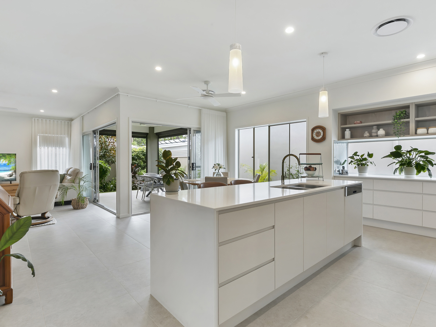 white kitchen interior with island bench overlooking indoor dining space and exterior rear patio