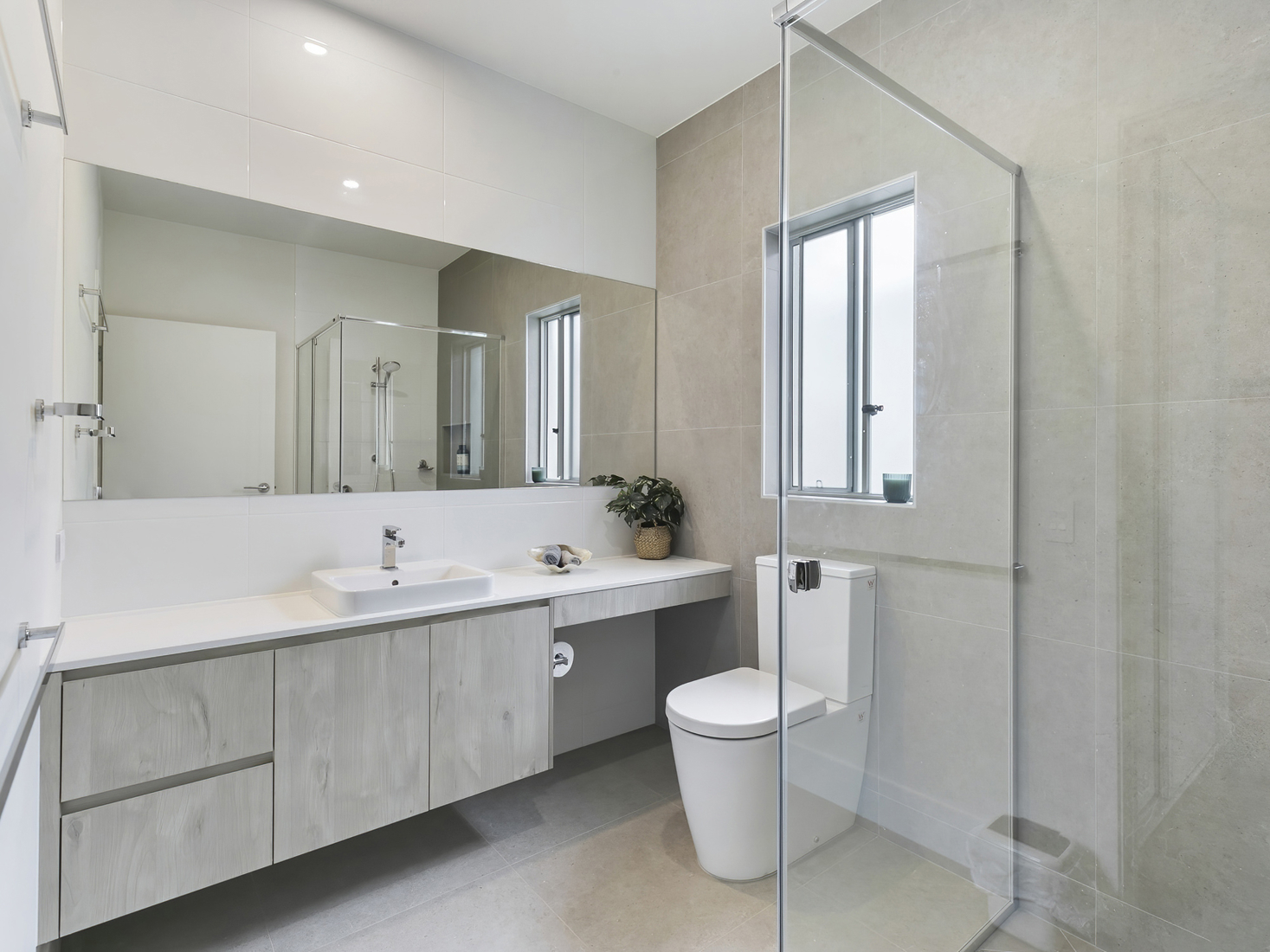 Modern established bathroom with full length vanity bench, glass shower screen and beige tiling.