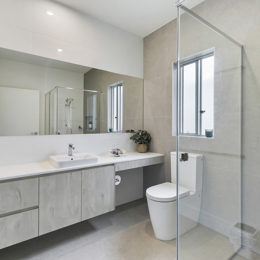 Modern established bathroom with full length vanity bench, glass shower screen and beige tiling.