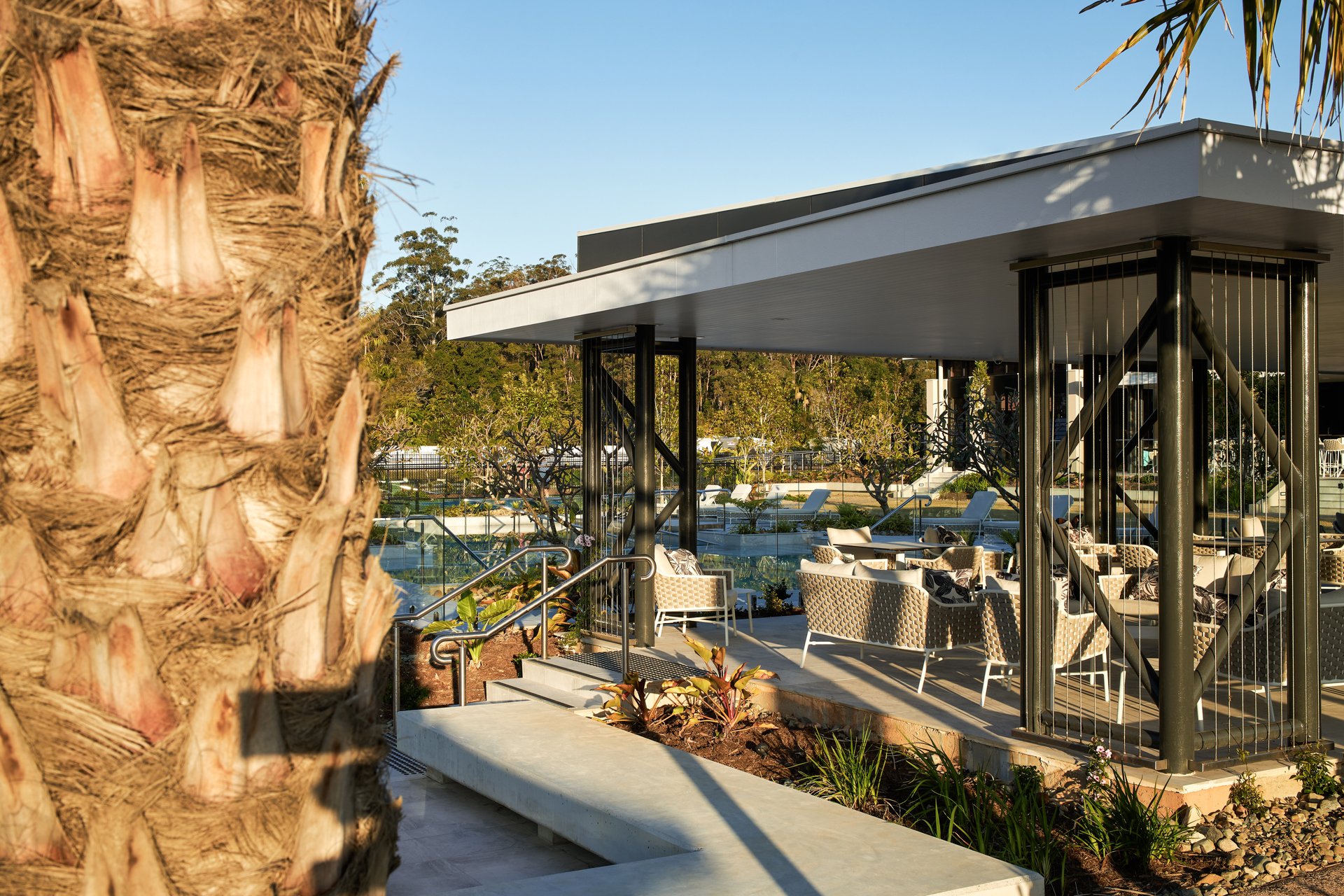 An image of the exterior corner of an outdoor pavilion with undercover seating overlooking tropical gardens.