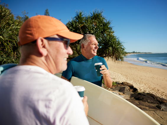 two men sit side by side whilst holding a coffee overlooking a Caloundra beach