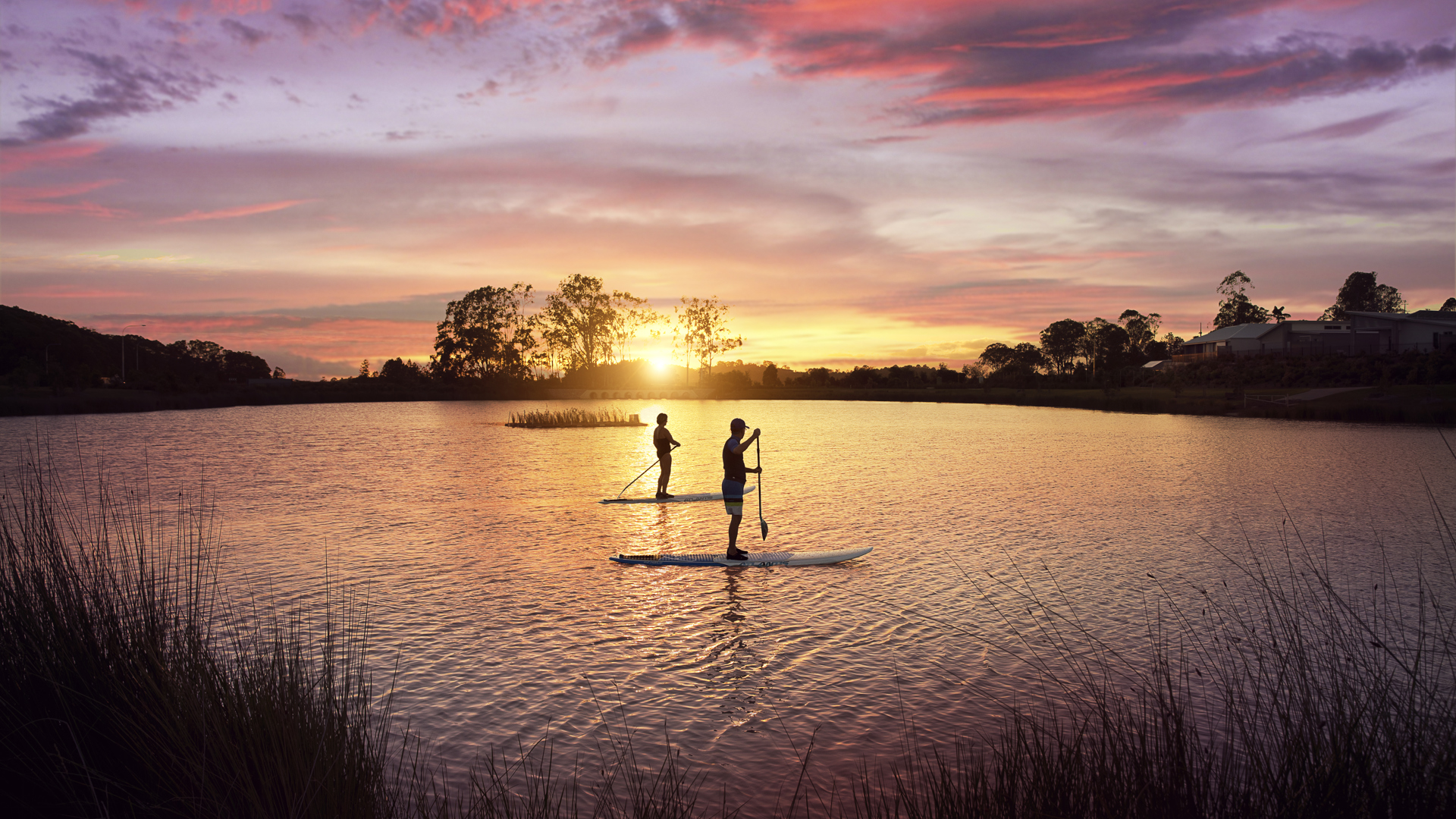 Two people on stand up paddle boards in the Halcyon Lakeside lake at sunset 
