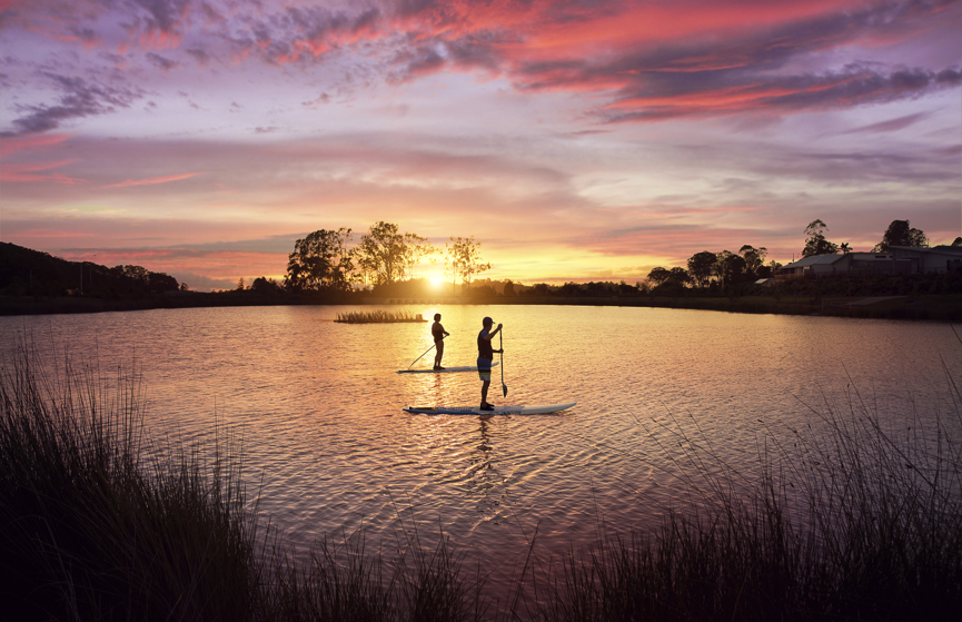 Two people on stand up paddle boards in the Halcyon Lakeside lake at sunset 