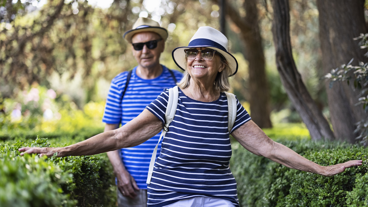 Stock image of a couple walking through a garden feeling the hedges. 
