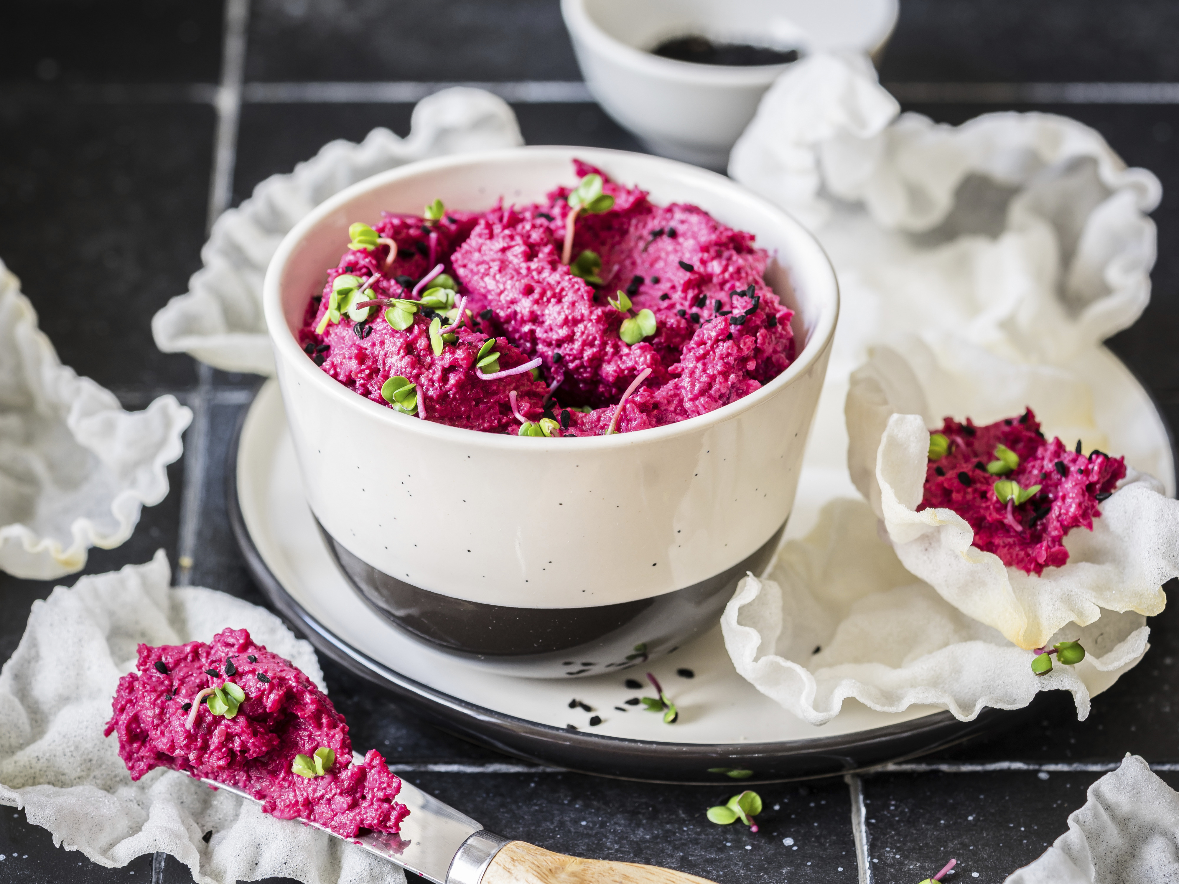 Bright beetroot hummus in a bowl topped with black sesame seeds.