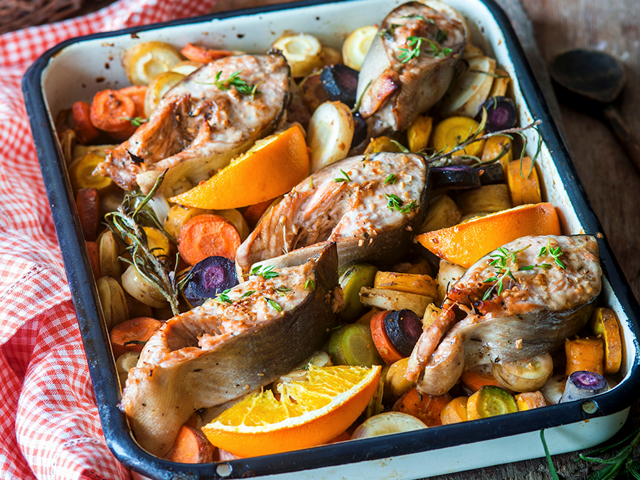 Roast salmon with rosemary, orange wedges and carrots in a oven tray.