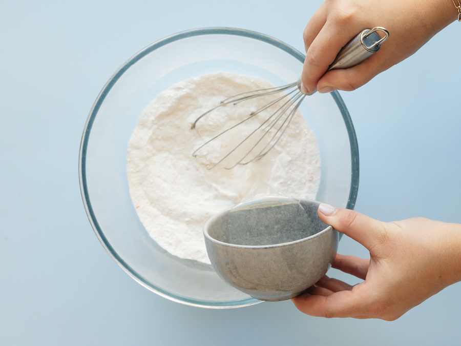 A glass mixing bowl with bi-carb soda, citric acid, and tartar being mixed with a whisk. 
