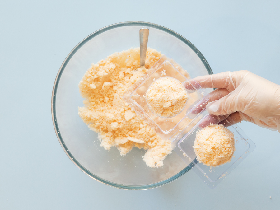 A glass mixing bowl with DIY bath bomb mixture. Some of the mixture is being packed into round ice cube tray moulds.