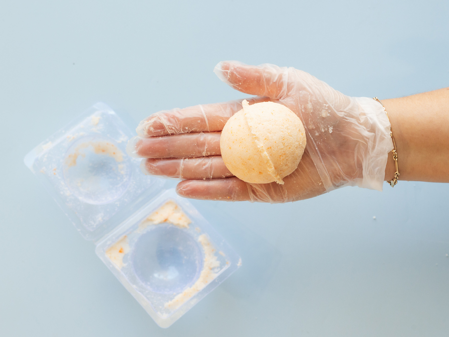 An orange coloured DIY bath bomb in the palm of someone's hand. 