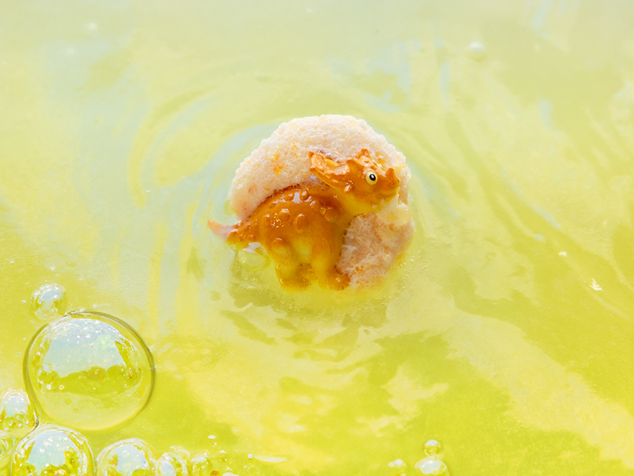 A DIY bath bomb foaming in a bath tub to reveal a hidden dinosaur figurine. 