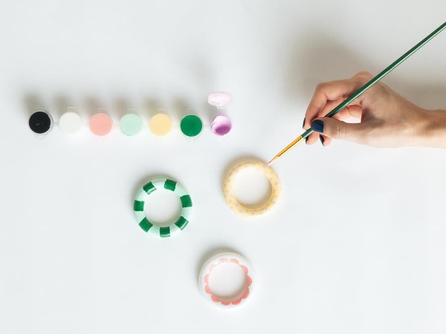 Someone's hand holding a paintbrush, painting round mini photo frames.