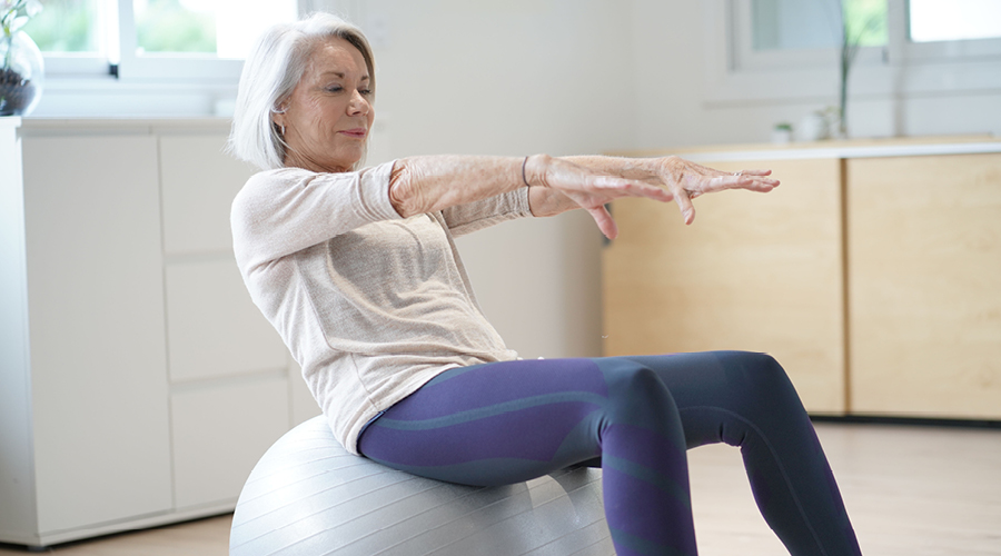 Older woman working out on a fitness ball at home.