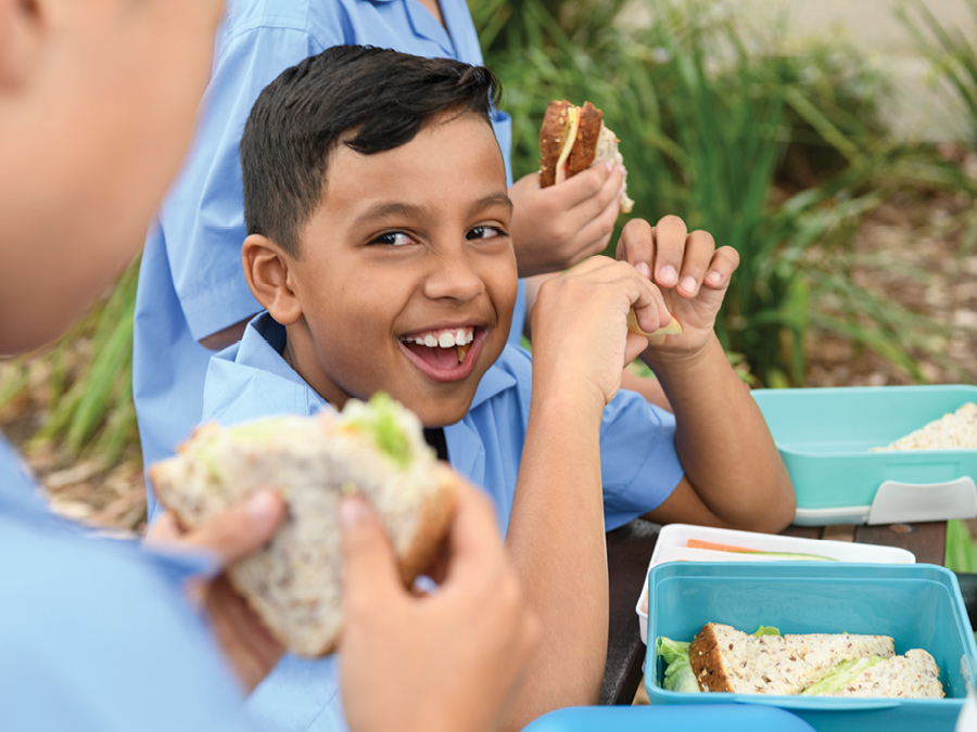 A school student eating his lunch with a smile on his face.