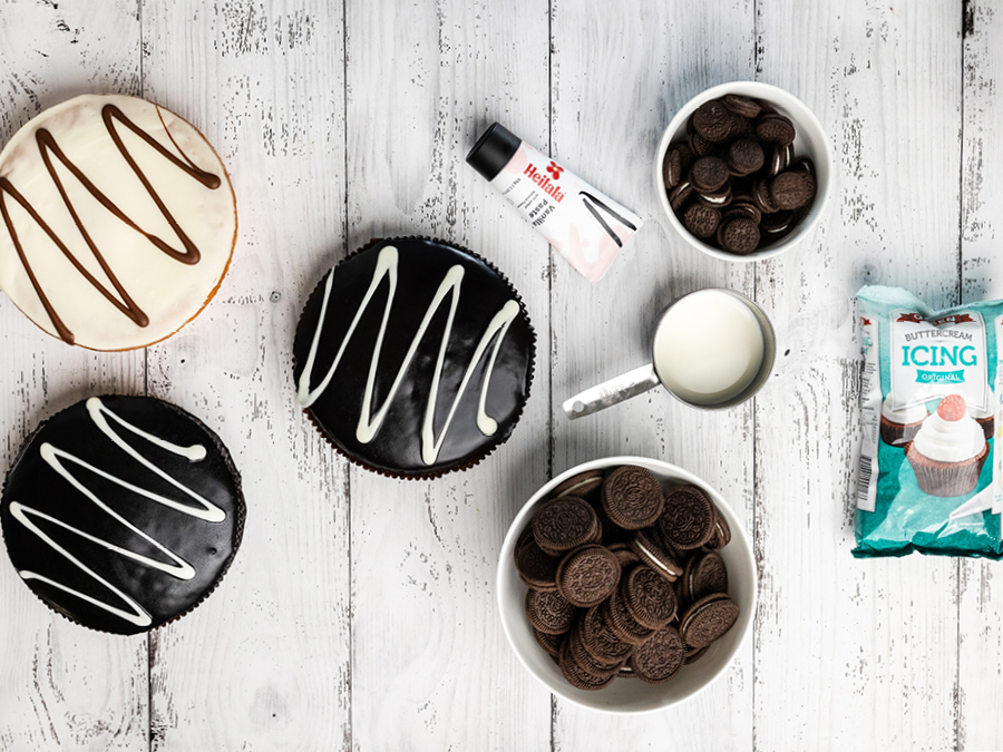 Three store bought chocolate mud cakes sitting on a white wooden bench with bowls of Oreos. 