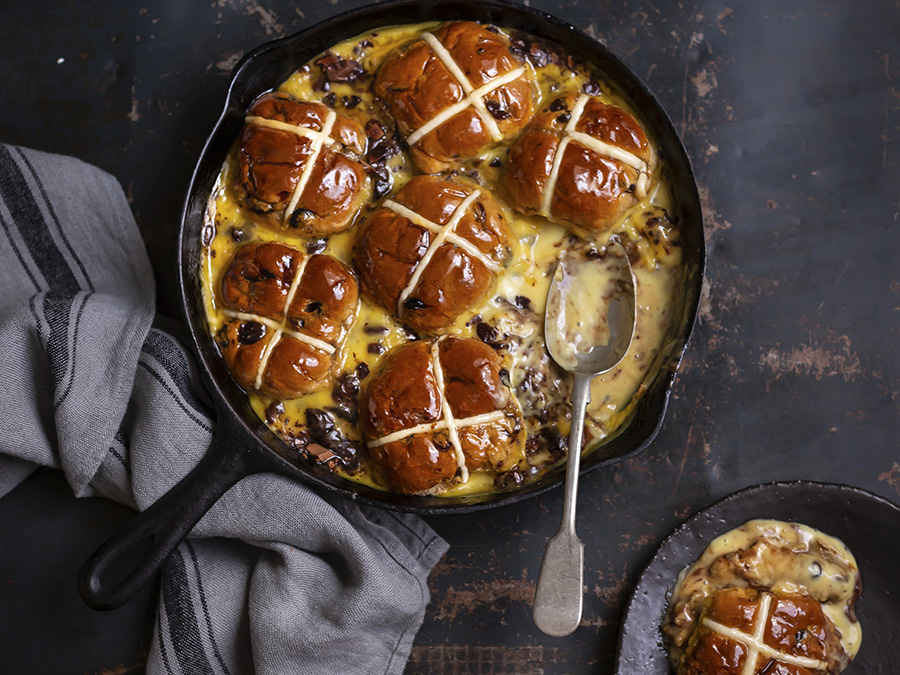 Hot cross bun pudding served in a cast iron pan on a black kitchen bench. 