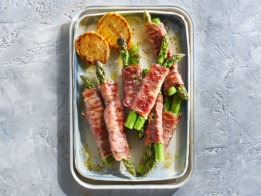 Asparagus wrapped in prosciutto and served on a baking tray.