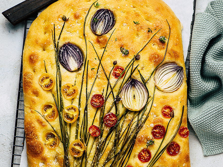 Baked garden focaccia bread with cherry tomatoes and red onion served on a baking tray.