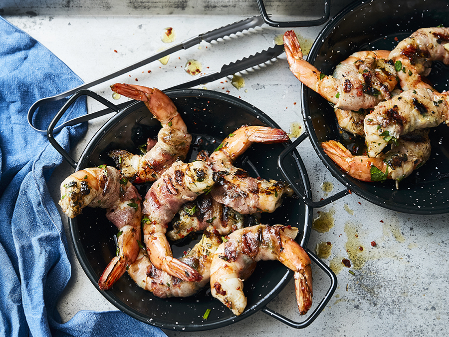 6 grilled prawns wrapped in bacon with herbs and served in a cast iron pan.