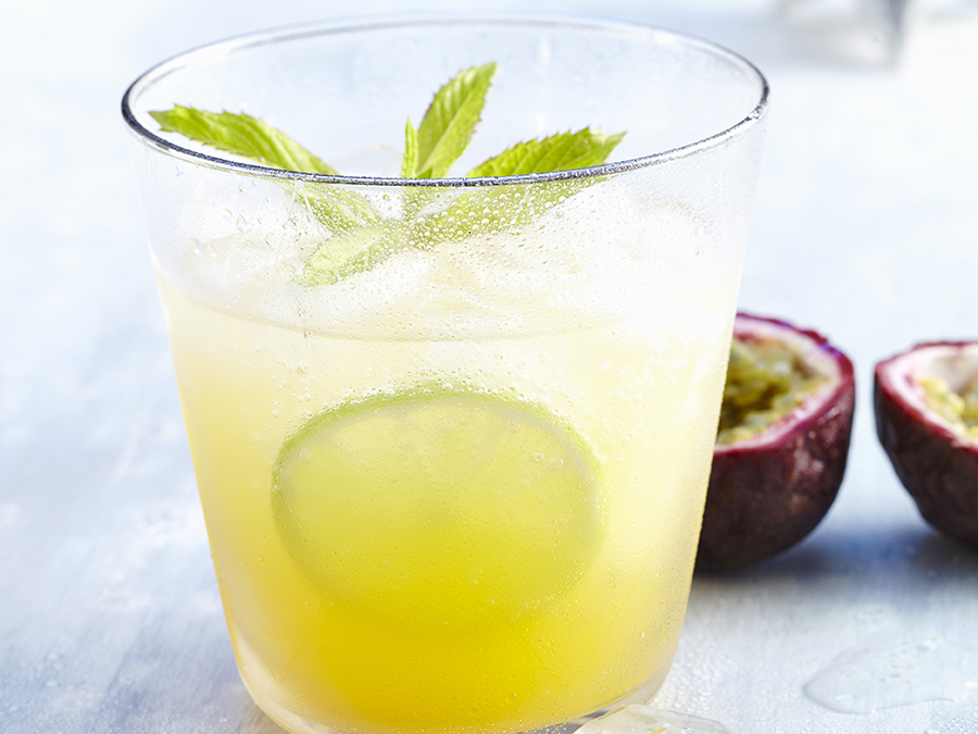 A glass of a non-alcoholic passionfruit spritz with a lime slice and topped with a sprig of mint. 