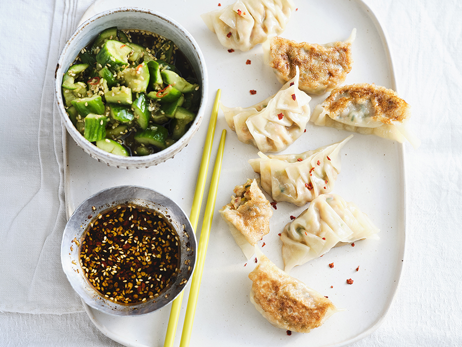 Japanese prawn and cabbage gyoza served with chilli flakes, and cucumber salad on a white plate.
